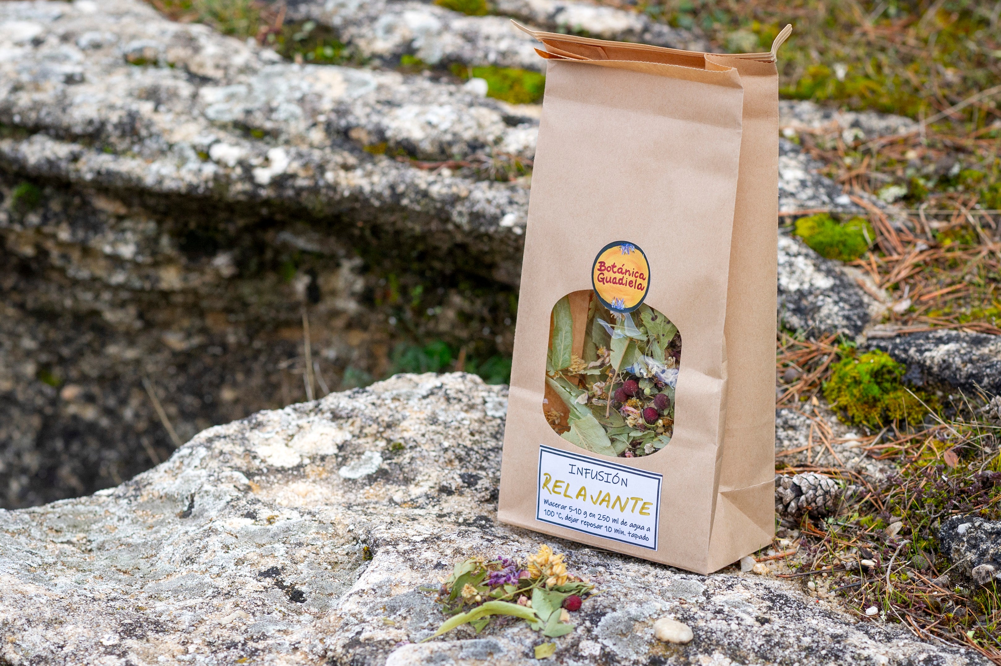 Bolsa de papel kraft con infusión Relajante artesanal de Botánica Guadiela, mezcla de flores y hojas silvestres sobre roca natural.